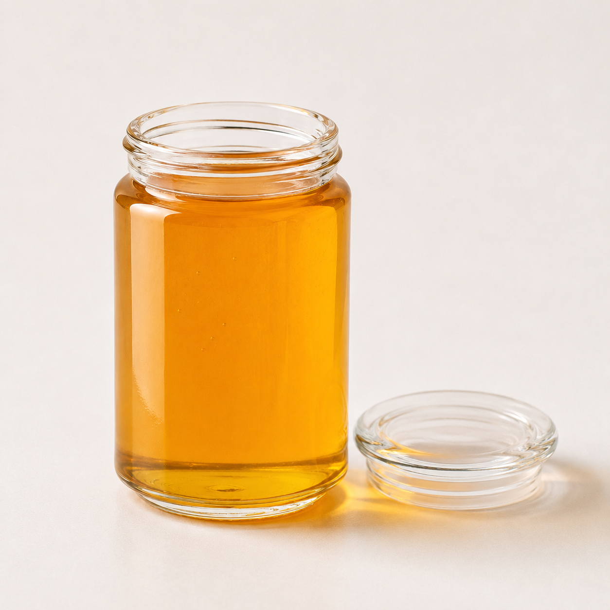 Open glass honey jar with matching clear glass lid
