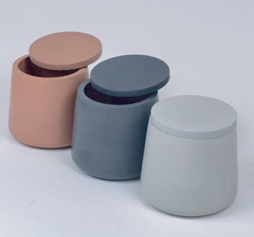 Muted ceramic candle jars with matching flat lids Pink, dark gray and pale blue round vessels with matching flat lids.
