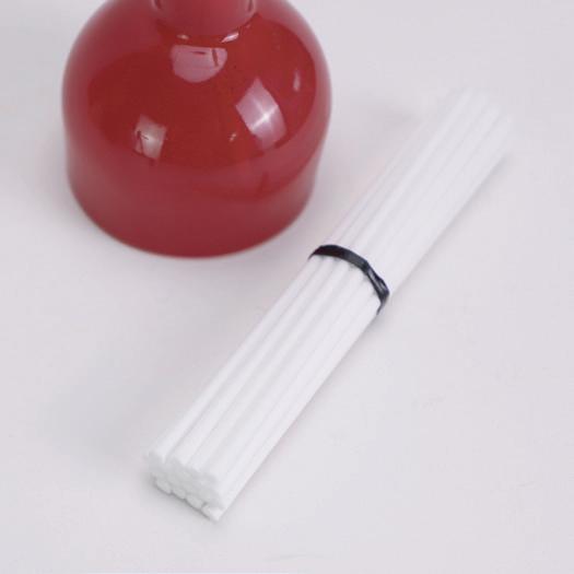 Bundle of white diffuser sticks beside a red glass bottle Bundle of white diffuser sticks beside a red glass bottle