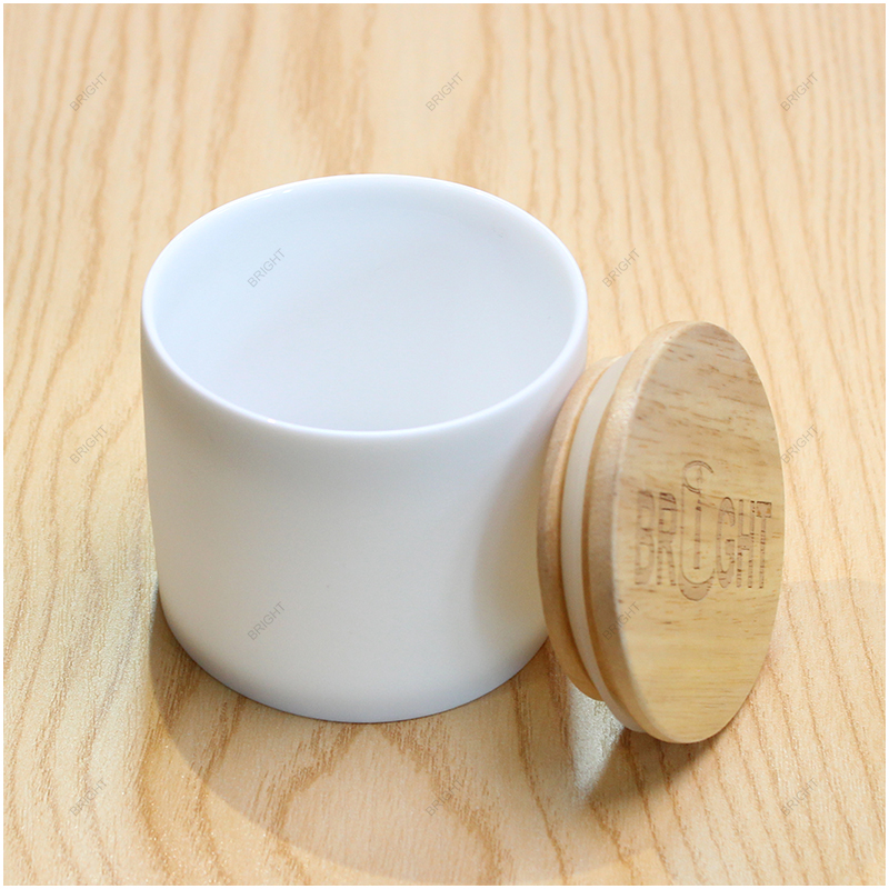 White ceramic candle jar beside a wood lid White jar and separate natural-colored lid on a wood-grain surface.