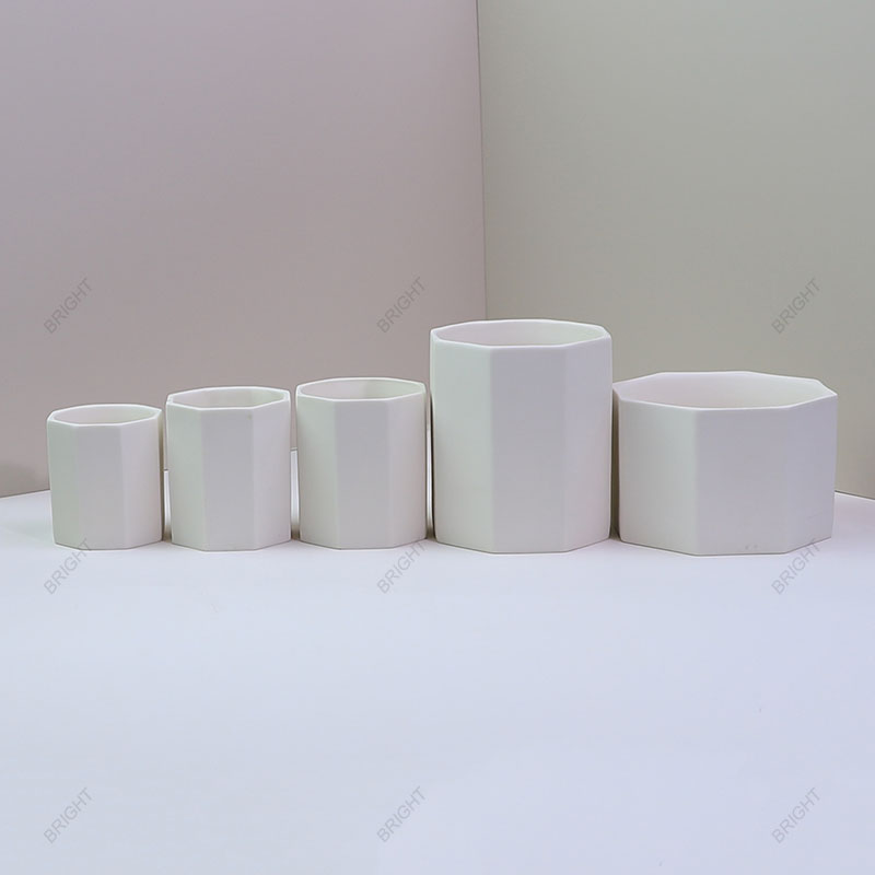 White faceted ceramic candle vessels in a range of proportions White round and faceted vessels arranged in several sizes.