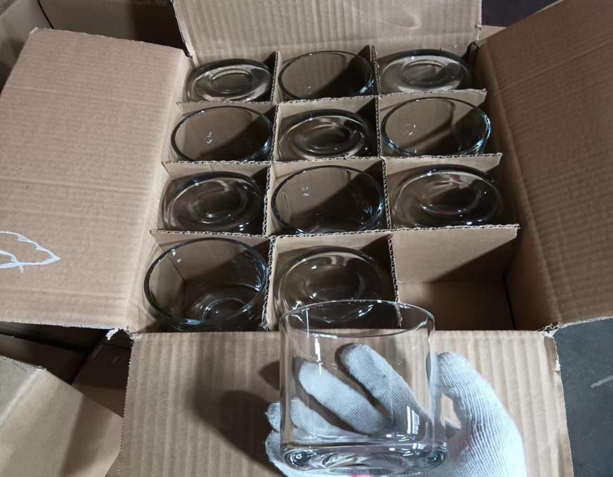 Clear glass candle jars separated by cardboard dividers in an open carton