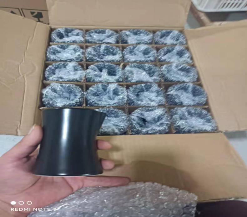 Unbranded ceramic candle jar beside individually protected vessels in a divided carton A dark vessel held above an open carton of individually wrapped containers.