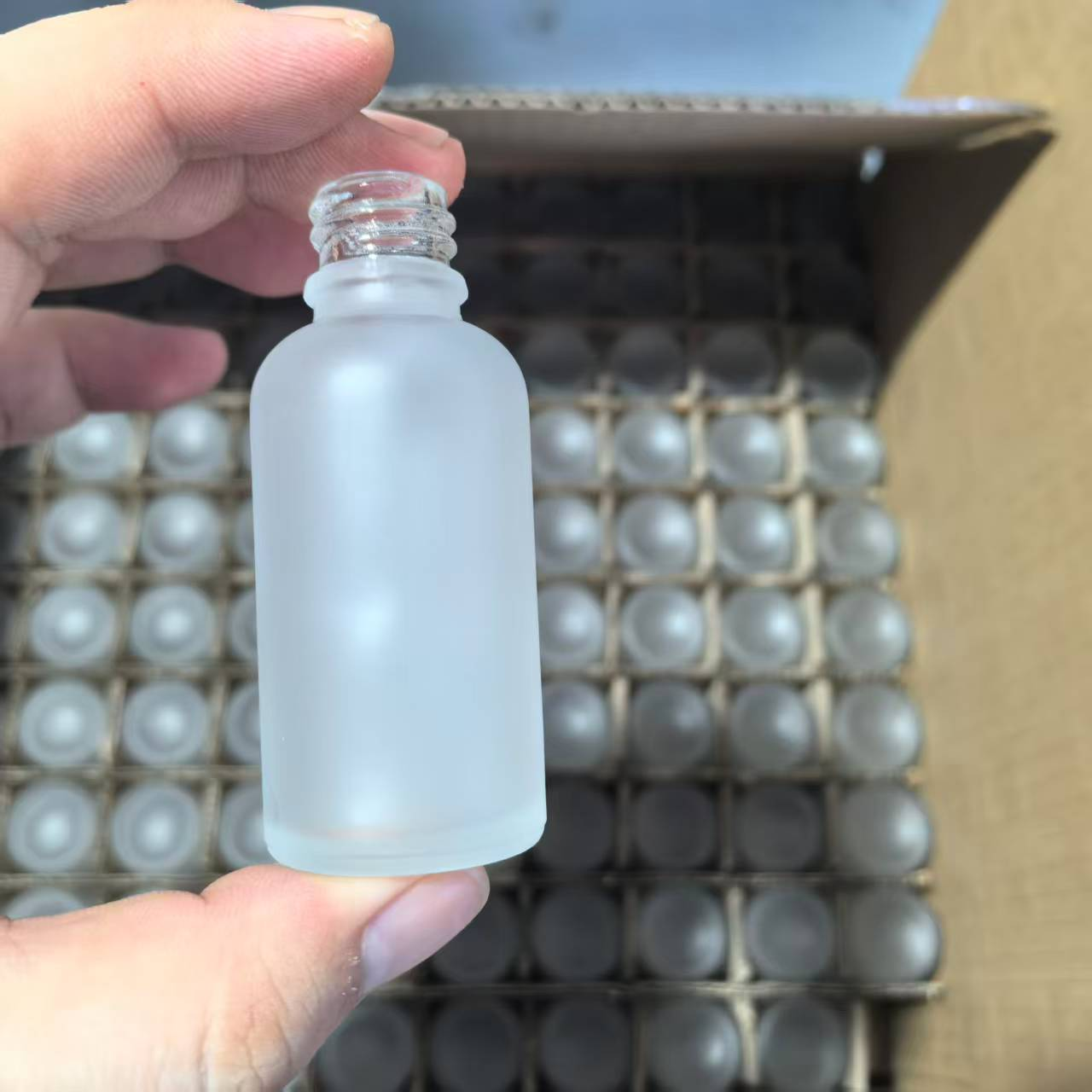 Hand holding a glass bottle with a frosted body and clear screw neck