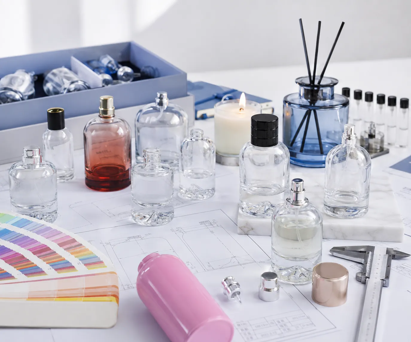 Rapid glass packaging samples and prototyping workspace with perfume bottles, diffuser bottle, candle jar, drawings, color swatches and measurement tools